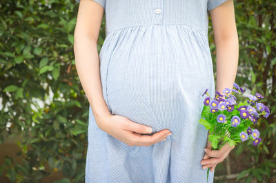 Midsection of pregnant woman holding flowers while standing at park