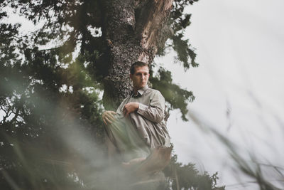 Low angle portrait of man sitting on tree