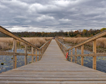 Boardwalk leading towards footbridge against sky