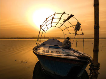 Fisherman sitting on boat moored at beach against orange sky