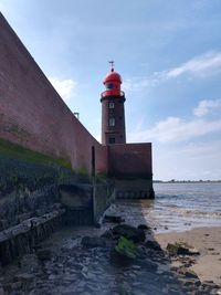 Lighthouse amidst sea and buildings against sky