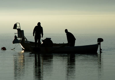 Silhouette man on boat in sea against sky