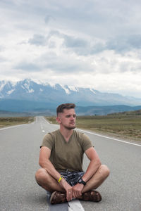 Portrait of young man sitting on road against sky