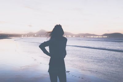 Rear view of woman standing on beach during sunset