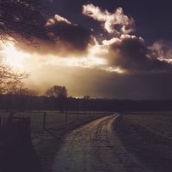 Road passing through field against cloudy sky
