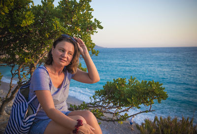 Mature woman sitting by tree at beach
