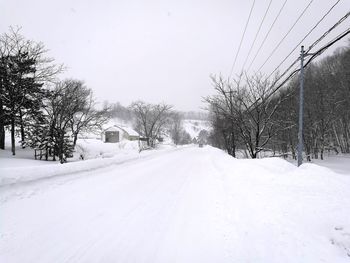 Snow covered road by trees against sky