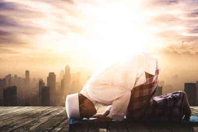 Side view of man sitting on terrace against sky during sunset