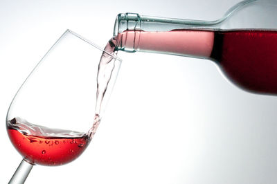 Close-up of red wine pouring from bottle in glass against white background