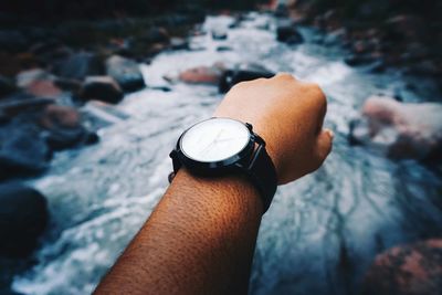 Cropped hand wearing wristwatch against river