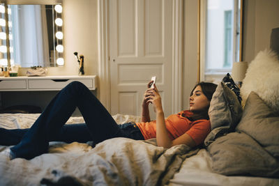 Girl using mobile phone while lying on bed at home