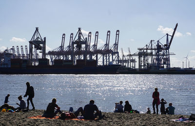 Silhouette people sitting on harbor against sky