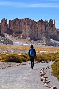Full length rear view of man standing on rock against sky