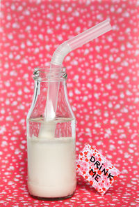 Close-up of milk bottle with drinking straw on pink table