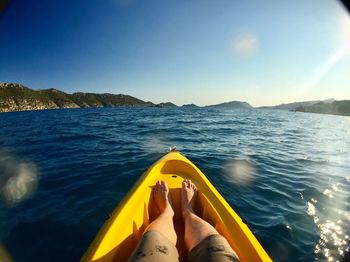 Low section of man sitting in boat on sea against blue sky