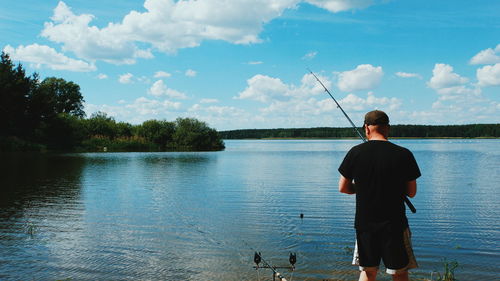 Rear view of man fishing in lake against sky