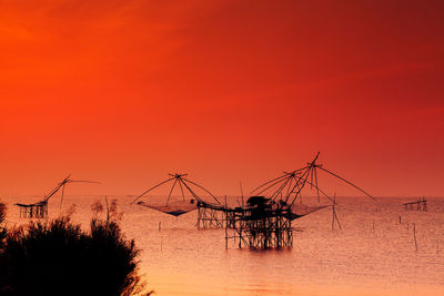 Chinese fishing nets in sea against sky during sunset