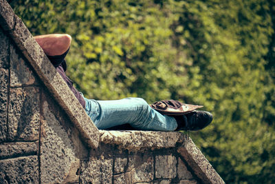 Low section of man relaxing on stone wall against plants