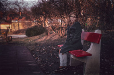 Portrait of young woman sitting on bench by footpath at park