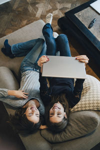 High angle view of smiling girls using laptop while resting on sofa at home