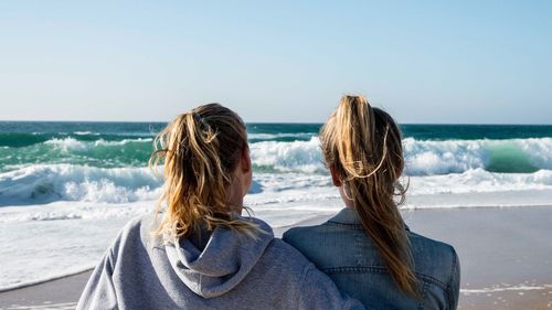 Rear view of friends at beach against clear sky