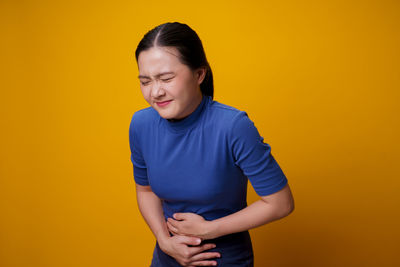 Young woman looking away while standing against yellow background