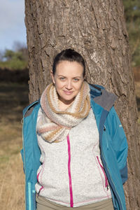 Portrait of beautiful woman standing against tree trunk