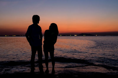 Rear view of silhouette couple standing at beach during sunset