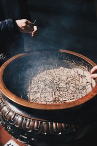 High angle view of woman holding incense stick standing by container at temple