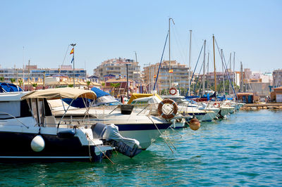 Boats moored at harbor against clear blue sky