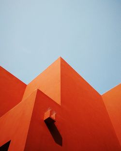 Low angle view of orange building against clear blue sky