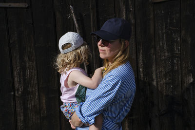 Girl wearing hat standing against wood