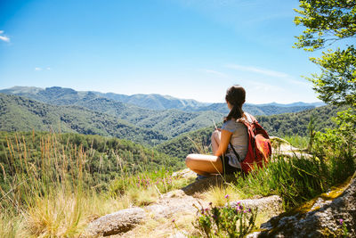 Rear view of woman sitting on landscape against mountain