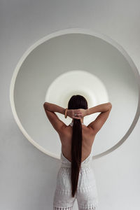 Rear view of woman with arms raised standing against white wall