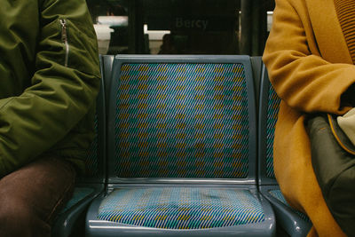 Midsection of people sitting on seats at subway station