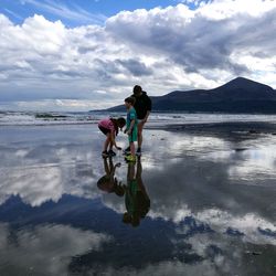 Family standing at beach against cloudy sky