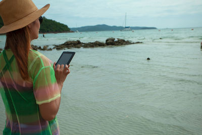 Woman using digital tablet while standing at beach