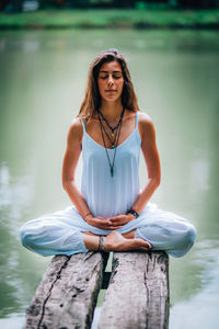 Woman doing yoga while sitting on pier at lake