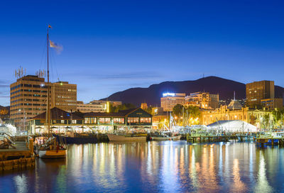 Sailboats moored on river by buildings in city at night