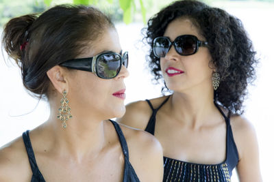 Portrait of two sister women wearing sunglasses against a river with trees in the background. 