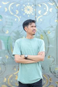 Young man looking away while standing against wall