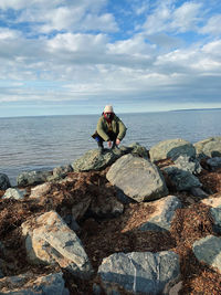 Front view of man sitting on rock by sea against sky