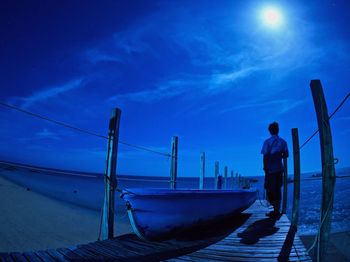 Rear view of man standing on jetty against blue sky