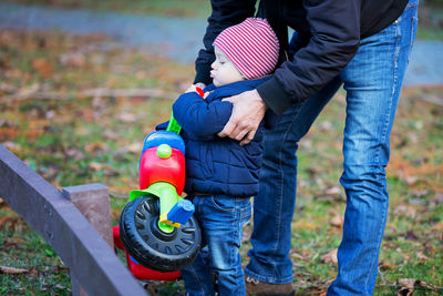 Midsection of father assisting son to carry tricycle