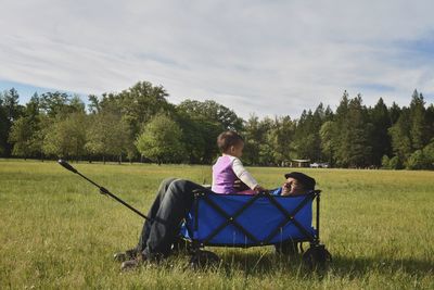 Woman sitting on field by trees against sky