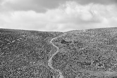 Scenic view of arid landscape against cloudy sky