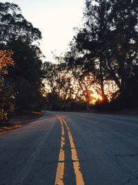 Road passing through forest at sunset