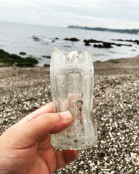 Close-up of hand holding glass of water on beach