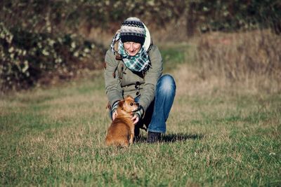 Portrait of smiling woman playing with dog on grassy field