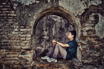 Side view of man sitting against wall